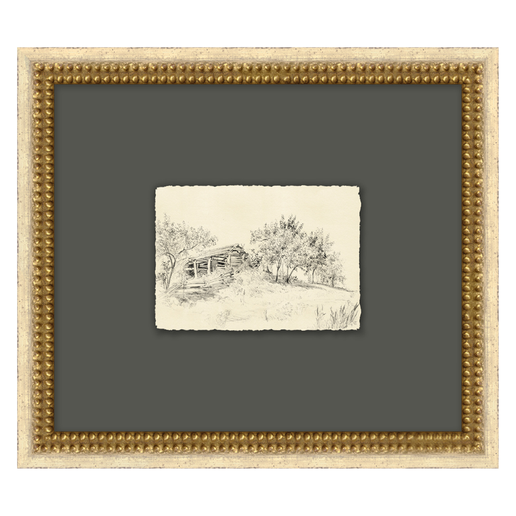Framed black and white landscape drawing of a cabin in the woods on gray paper.