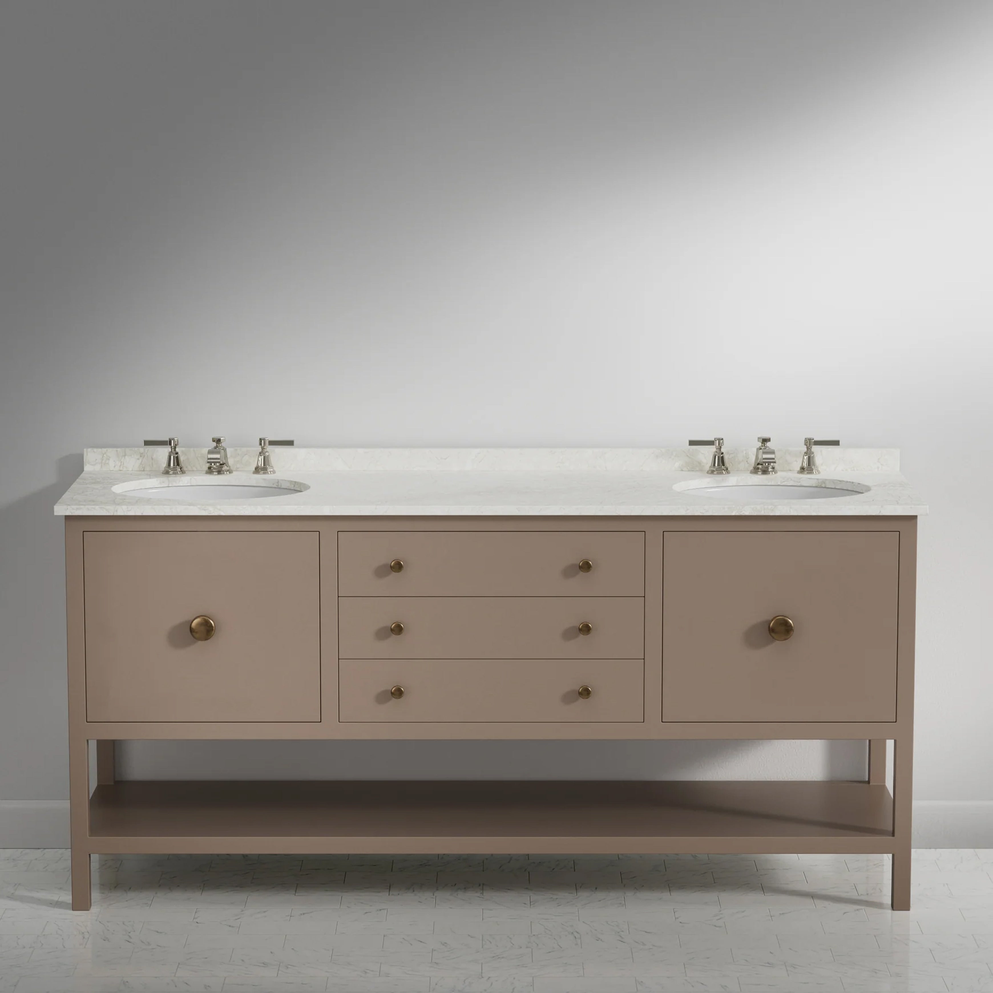 A double-sink bathroom vanity with a warm taupe-beige cabinet, a white countertop, and brass hardware, set against a neutral gray studio background.