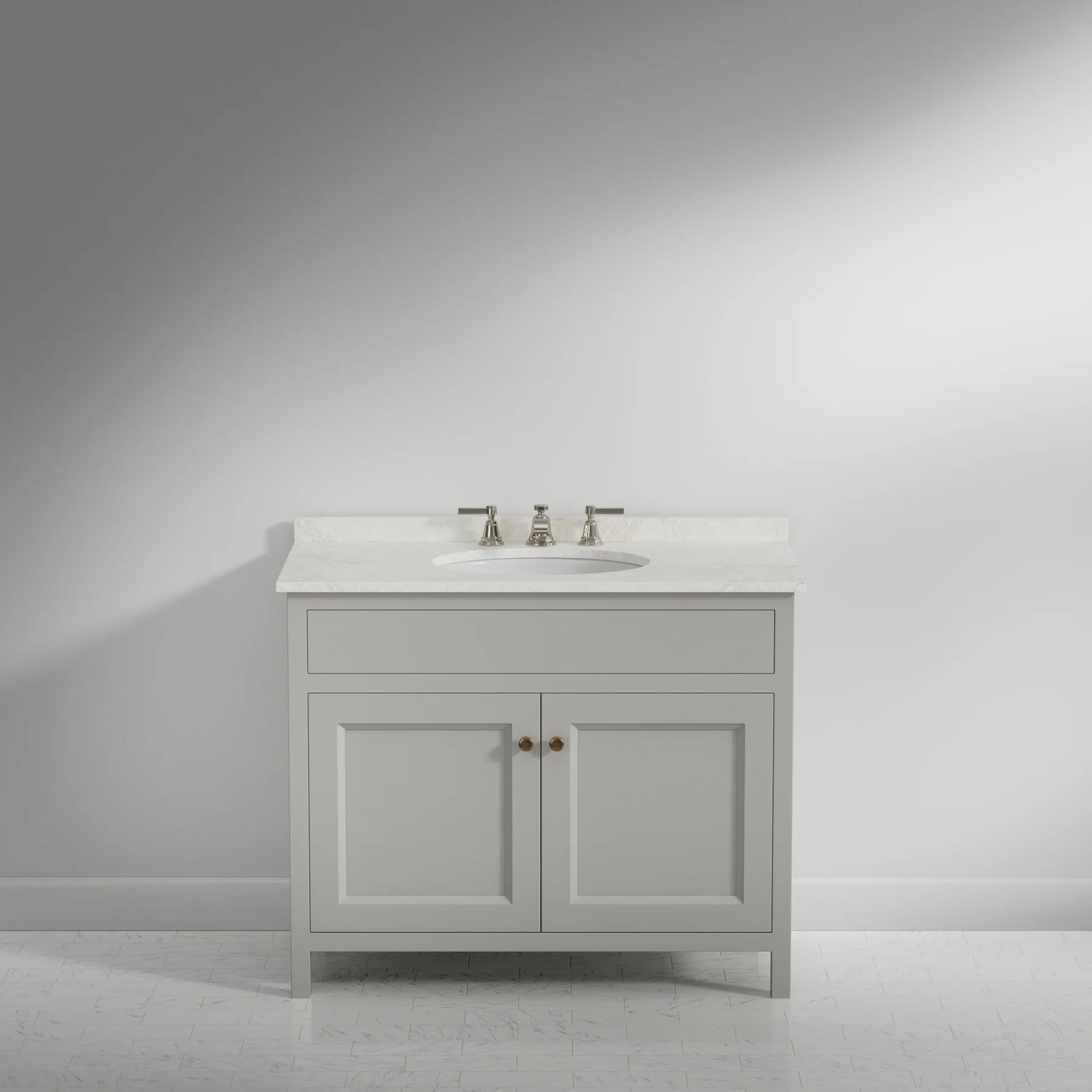 A single bathroom vanity cabinet with two doors, a white drawer, and an integrated white sink, shown against a light gray wall and floor. The cabinet has small round metallic knobs, and a chrome faucet and handles are mounted on the white countertop.