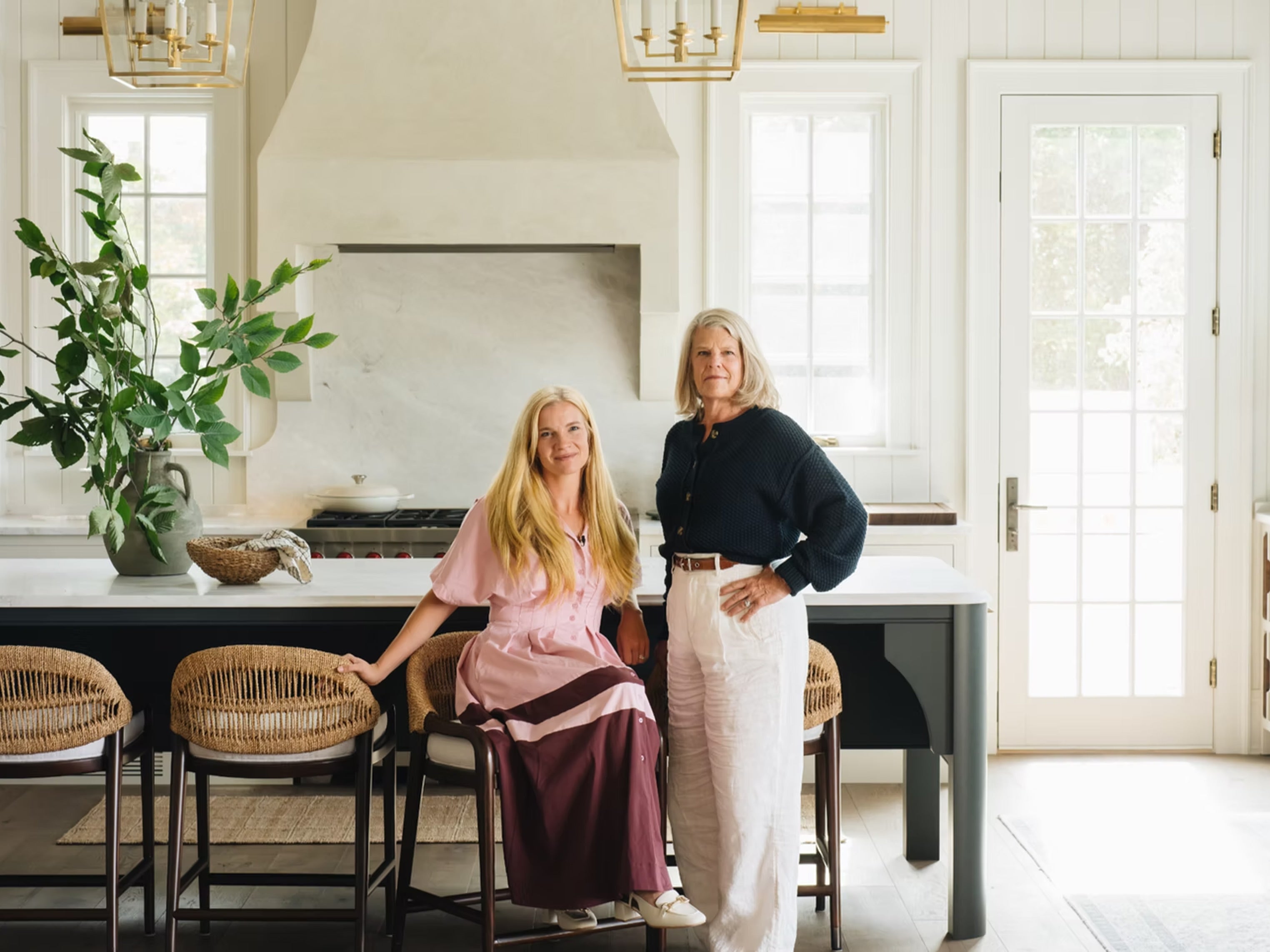 Two women standing in a modern kitchen with white cabinets and a large window.