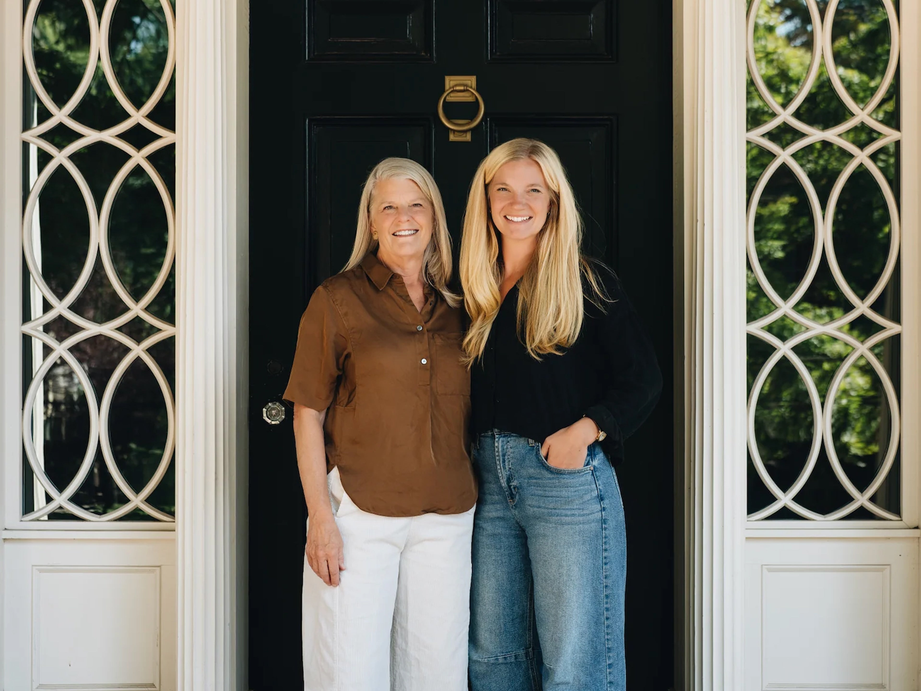 Two women standing in front of a black door with decorative glass panels.