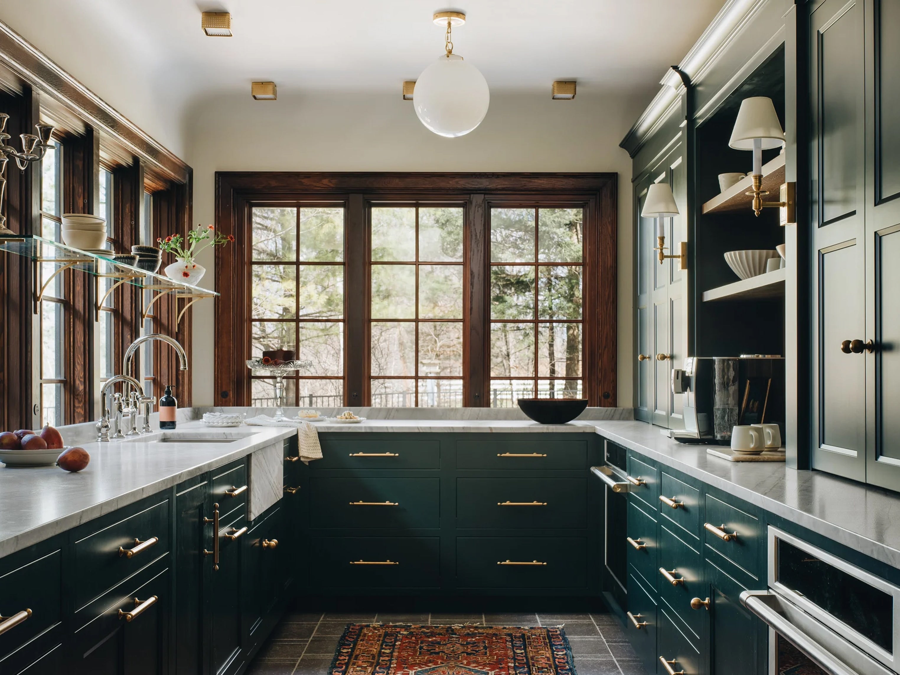 Modern kitchen with dark green cabinets, white countertops, and large windows.